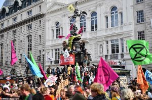 Extinction Rebellion eco protesters wave flags from the Shaftesbury Memorial Fountain at Piccadilly Circus in London